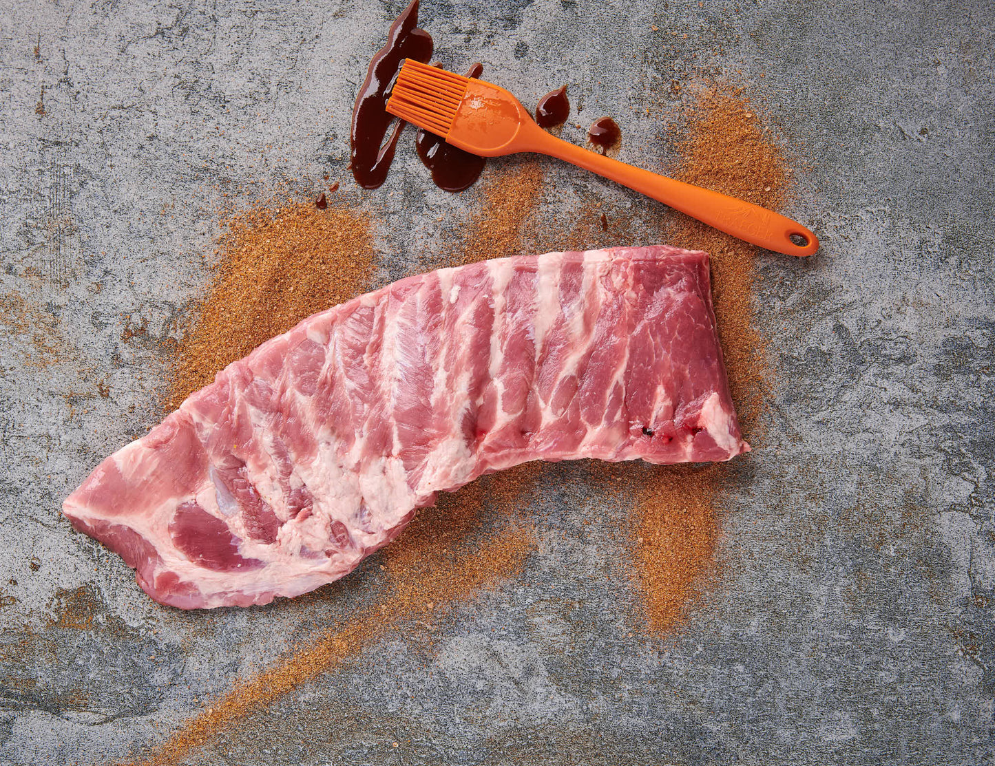 Spareribs im St. Louis Cut roh mit BBQ-Rub und Sauce-Pinsel auf Steinplatte