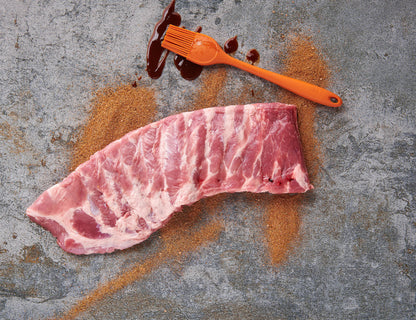 Spareribs im St. Louis Cut roh mit BBQ-Rub und Sauce-Pinsel auf Steinplatte